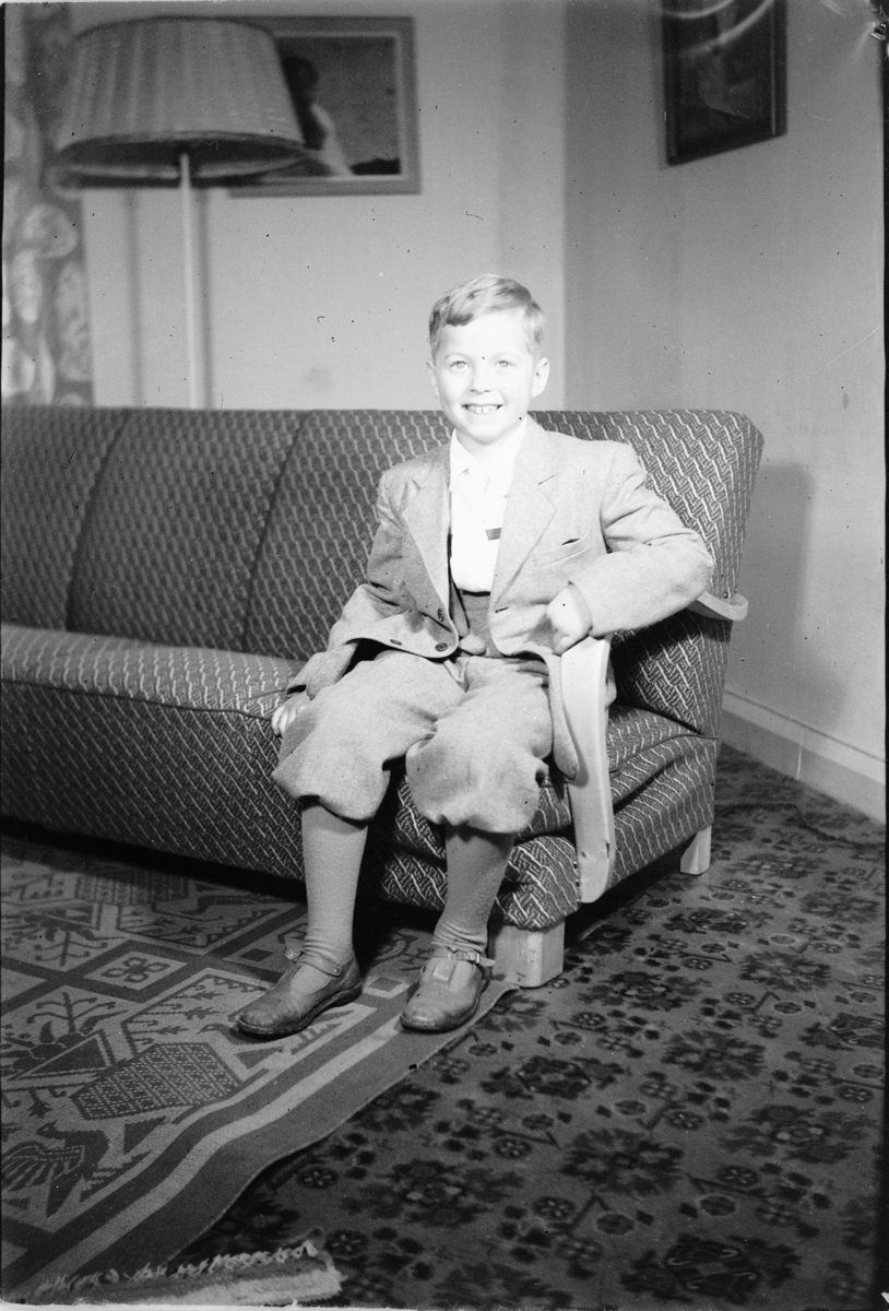 Håkon Prestkværn, Interiør, stue. En gutt sitter i en sofa.