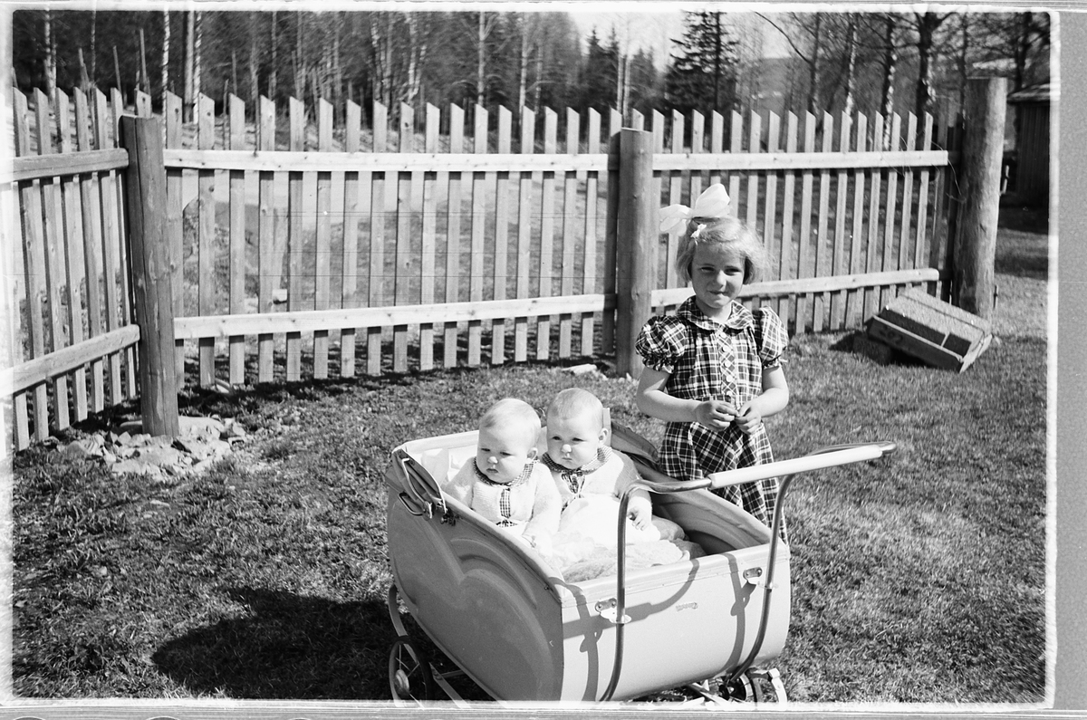 Håkon Prestkværn, Tvillingene i vogna er Knut og Bjørg Svenskerud f. 1949. Jenta med sløyfe er Inger Svenskerud f. 1945. Bildet er tatt ved Åsmarka kirkestue. Jente med sløyfe i håret og to babyer i barnevogn.