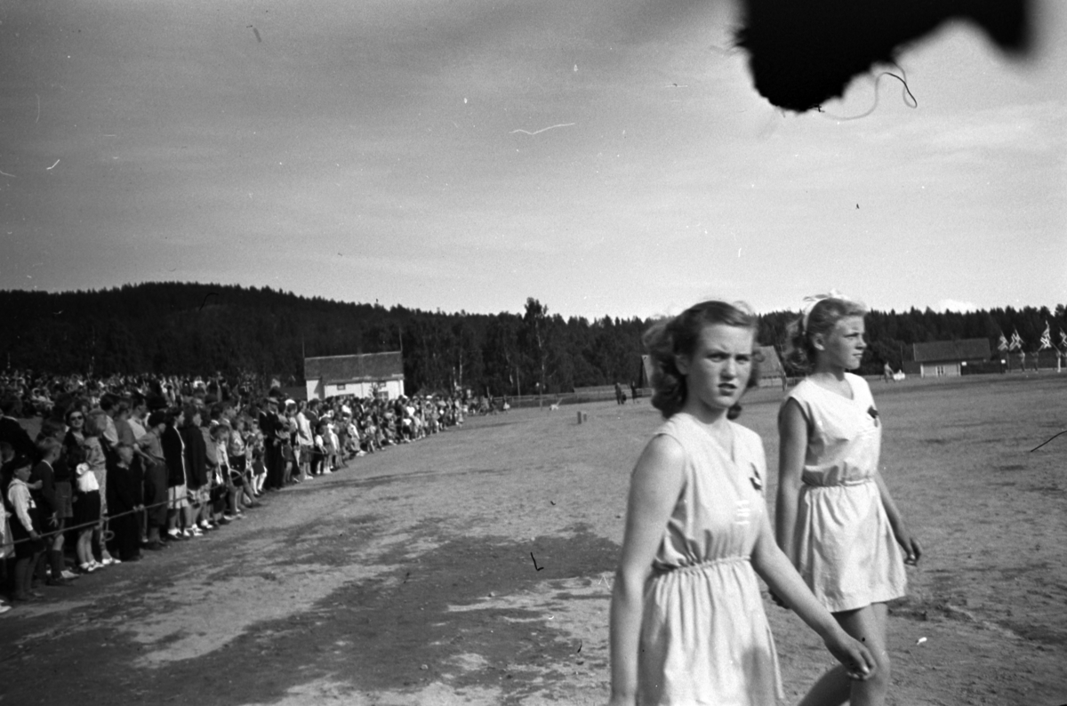 Håkon Prestkværn, To jenter med publikum i bakgrunnen på et turnstevne, Moelv Idrettspark, juni 1949.