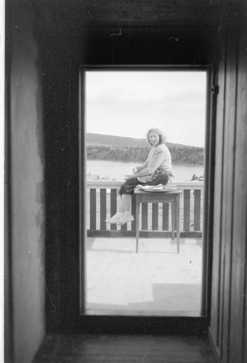 Håkon Prestkværn, Ukjent kvinne sitter på et bord på en veranda.