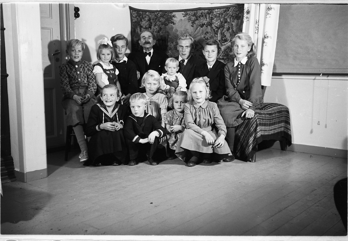 Håkon Prestkværn, Interiør, stue. Gruppe barn samlet rundt en eldre mann.