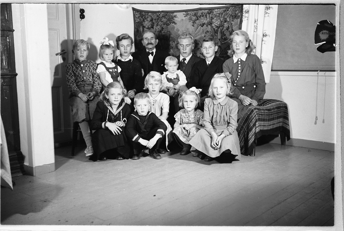 Håkon Prestkværn, Interiør, stue. Gruppe barn samlet rundt en eldre mann.