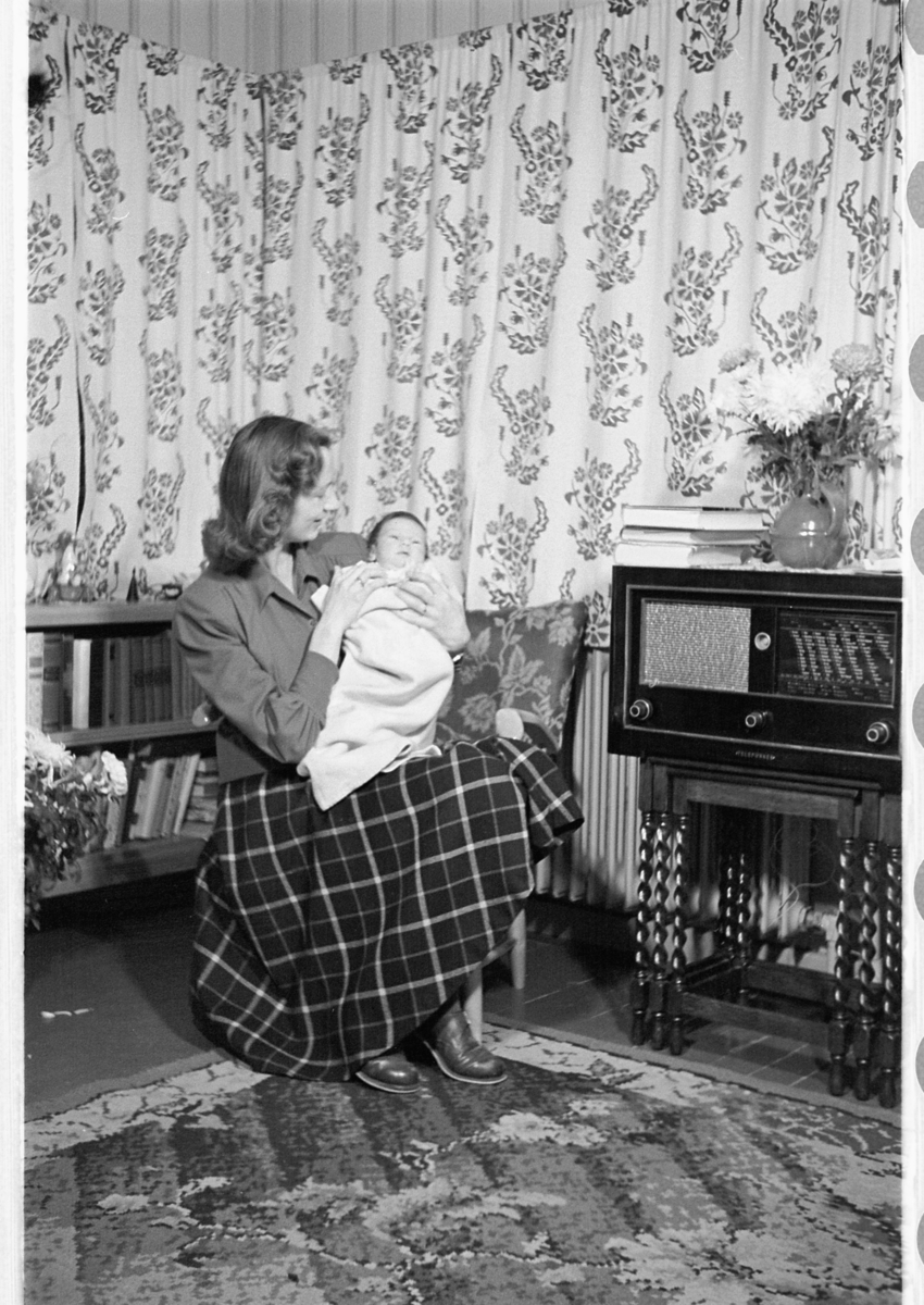 Håkon Prestkværn, Interiør, stue. Kvinne med en baby på fanget. Radio.