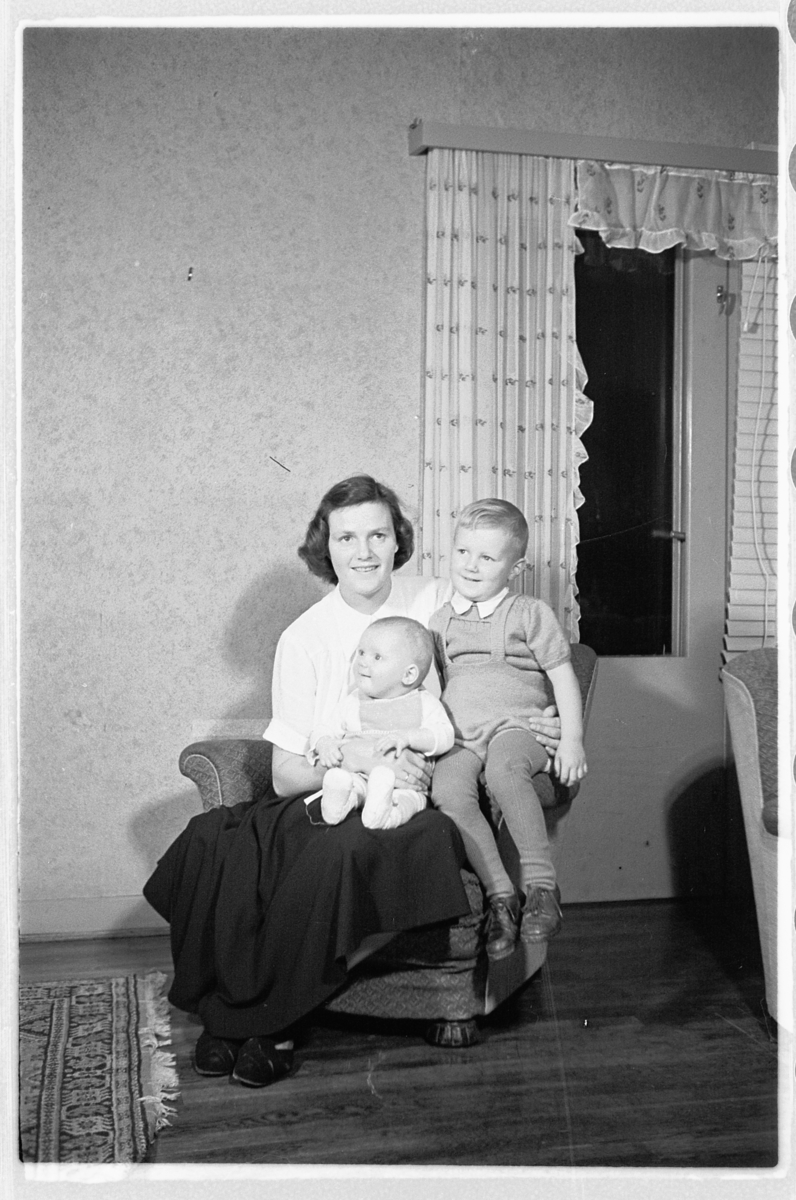 Håkon Prestkværn, Interiør, stue. Kvinne med en gutt og baby på fanget.