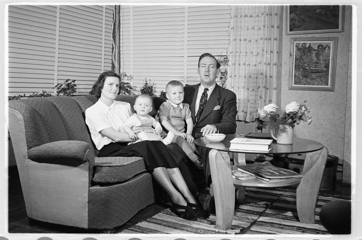 Håkon Prestkværn, Interiør, stue. Kvinne og mann i en sofa med en baby og en gutt.