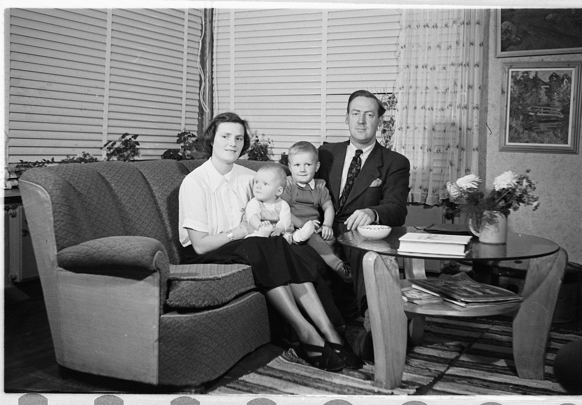 Håkon Prestkværn, Interiør, stue. Kvinne og mann i en sofa med en baby og en gutt.