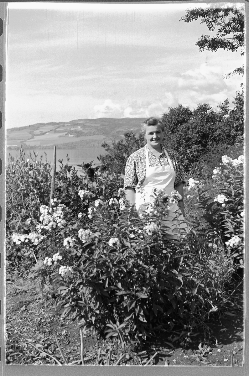 Håkon Prestkværn, Eksteriør, hage. Ukjent kvinn med forkle ved noen blomster.