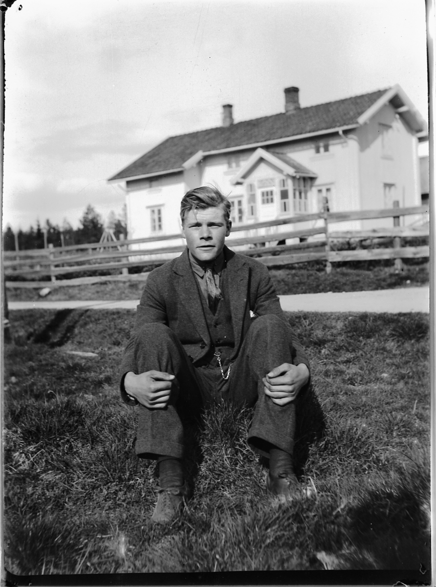 Ole M Martinsen, Ukjent mann sitter på bakken foran et hus med gjerde.