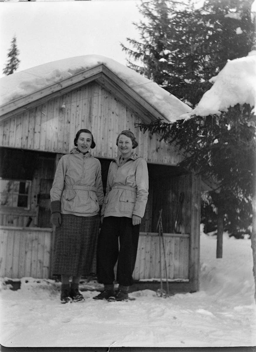 Ole M Martinsen, To kvinner foran ei HYTTE i skogen.