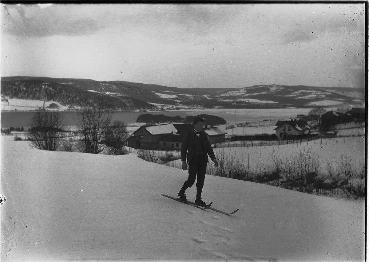 Kristoffer Horne, VINTERLANDSKAP PÅ RING i Ringsaker, MANN PÅ SKI. Østre Fjelstad i bakgrunnen.