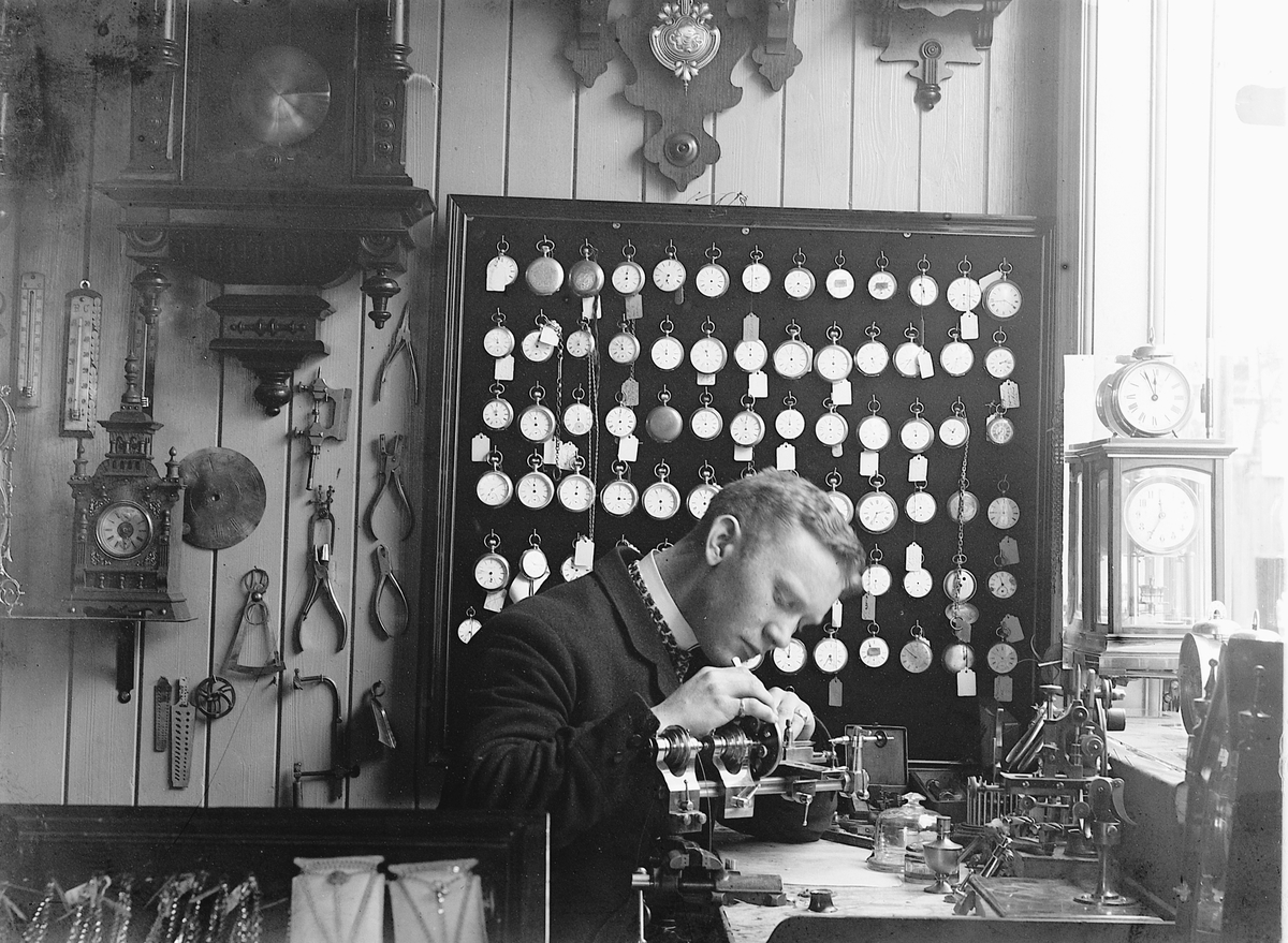 Ragnvald Andersen, Urmaker i arbeidet. Ur på veggen. Torggata 52, Hamar. Sjølportrett av Ragnvald Andersen. Interiør.