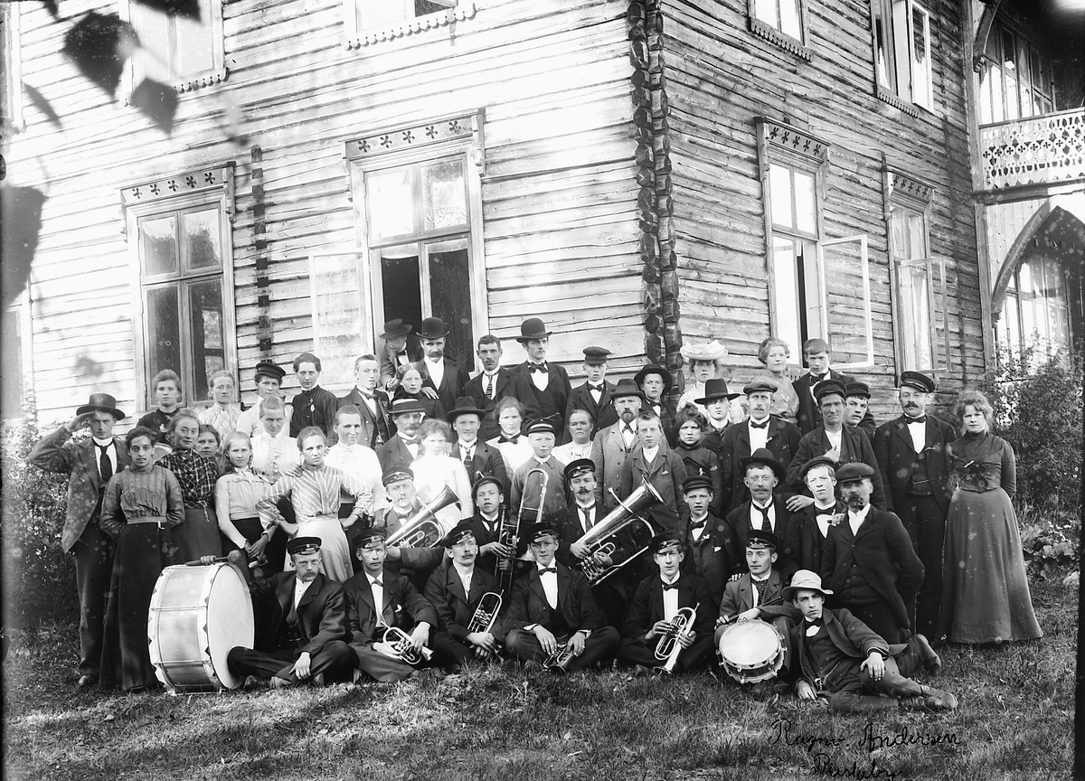 Ragnvald Andersen, Kjelsrud gård, Helgøya. Kokerimusikken med familie på tur. På siden av huset. Instrumenter.