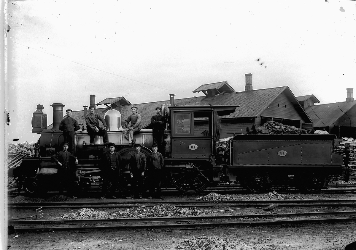 Ragnvald Andersen, Damplokomotiv på Hamar stasjon, nr 31, flere menn oppstilt. Rørosbanen. Lokomotiv 31, bygget i 1893 av Dübsachs i Glasgow og gikk på Rørosbanen til 1931. Foran fv: Ole Granberg, Ingvald Kristoffer Hansen, Lars Amundsen og Sigvart Trøndsen (Trondsen?). Bak: Peder Holen (Holm), Johannes Flagstad, Hal…