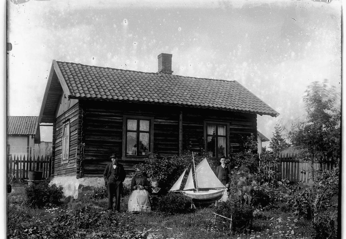 Ragnvald Andersen, Eksteriør, hus med hage. Ukjent mann, kvinne og to barn, en gutt med en seilbåt.