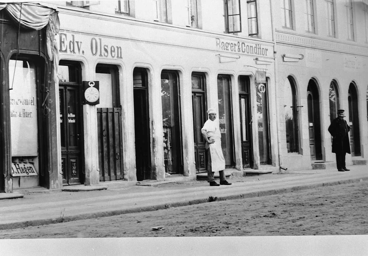 Hans Emil Erichsen, Strandgata 41-43 i Hamar. Forretningene til Emma Dahl, J.O. Hagen, Bager & Conditor Edv. Olsen, J.O. Lier og søstrene Lier. Personene på bildet er bakermester B. Opsahl og tannlege C. Opsahl.