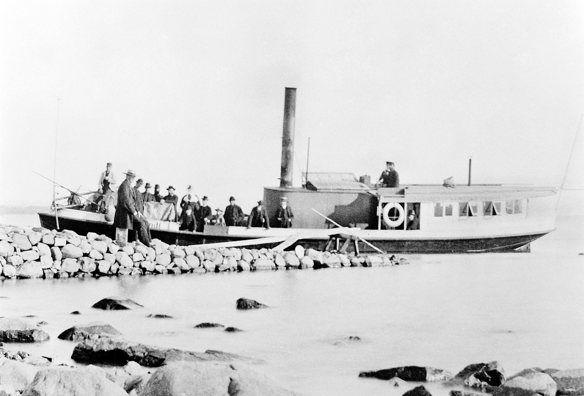 Hans Emil Erichsen, D/S Lettvindt ved Jessnes Brygge i Ringsaker. Kaptein Christian Jensen står i styrhuset. Mjøsbåt. Steinbrygge. Lettvindt var Mjøsas første propellbåt, bygd i 1867. Senere ble den ombygd og døpt Helgøy. Den endte sine dager ved Minnesund i 1960 under navnet Mira. Christian Jensen var forøvrig tidlig…