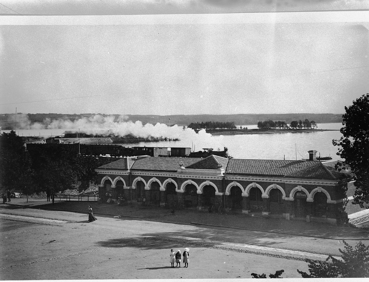 Hans Emil Erichsen, Stortorget, Hamar. Basarbygningen med et damptog i bakgrunnen. Basarbygningen sto ferdig i 1896.