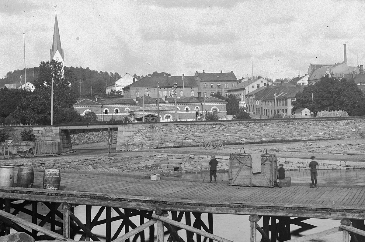 Hans Emil Erichsen, Hamar brygge med dyrekasser, sprittønner og melkespann. Basarbygningen i bakgrunn. Bebyggelsen rundt Stortorget.