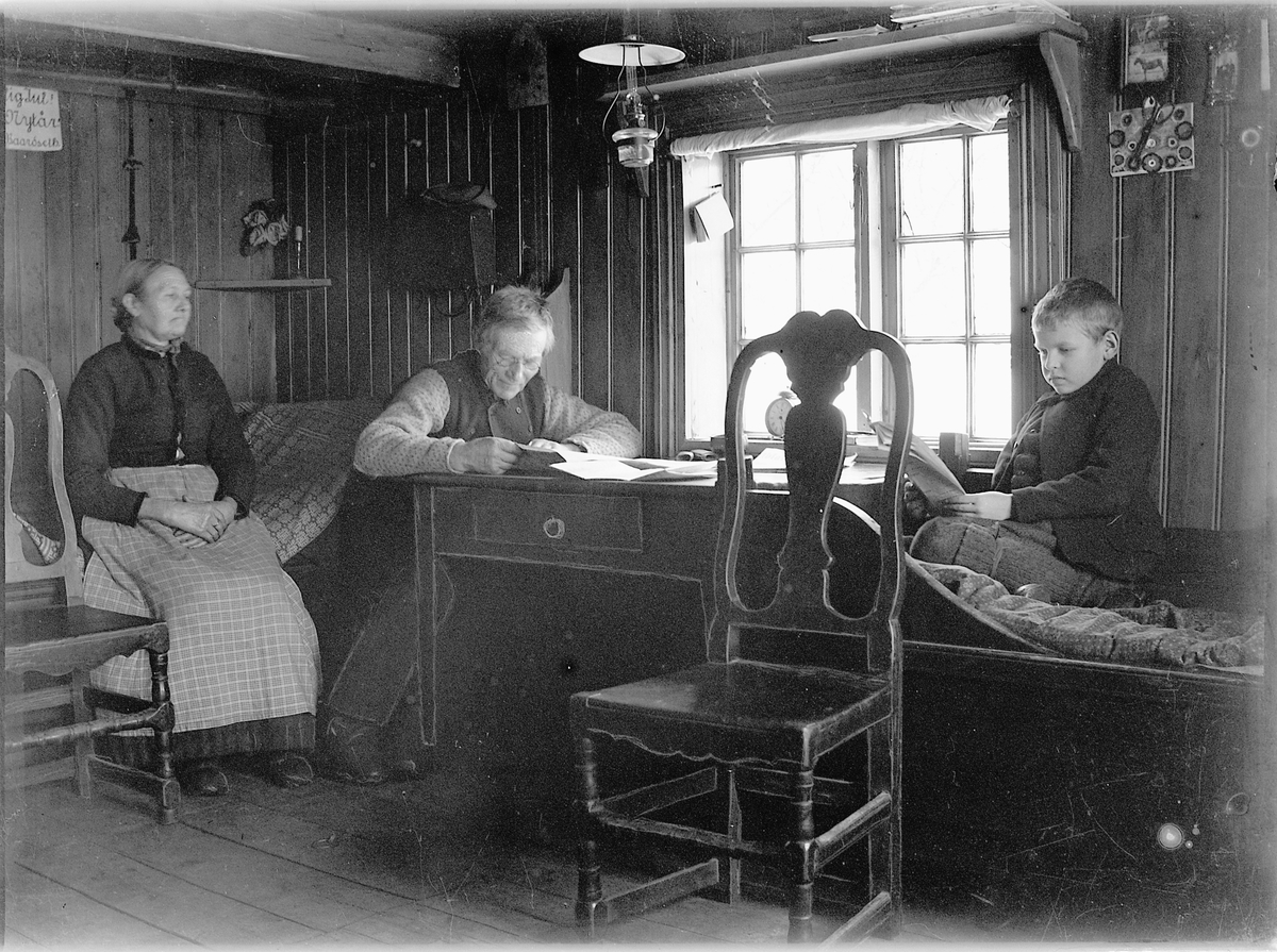 Simen Baardseth, INTERIØR FRA HUSMANNSPLASSEN STUGGULYKKJA UNDER BÅRDSET, KONA UKJENT, NILS LESER OG BARNEBARNET NICOLAI HAGEN LESER.