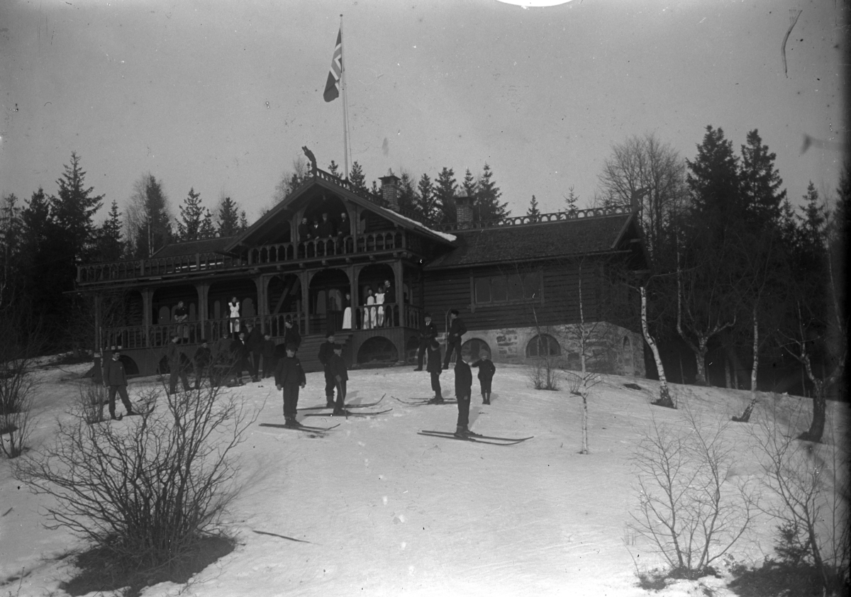 Johannes Larsen Alhaug, Skistua på Alhaug, Hamar. Ble bygget i 1898 av Peder Alhaug på Alhaug Østre, brant ned i 1921 men ble bygget opp igjen. Gruppe på ski utenfor.