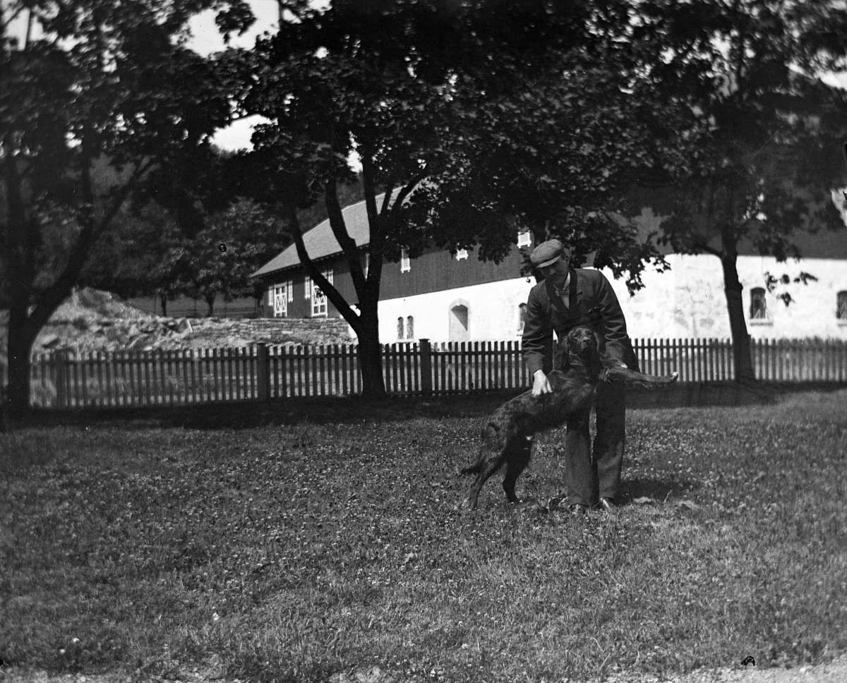 Martin Finborud, En mann med en hund i en hage. Fjøs i bakgrunnen. Johan E. Mellbye?