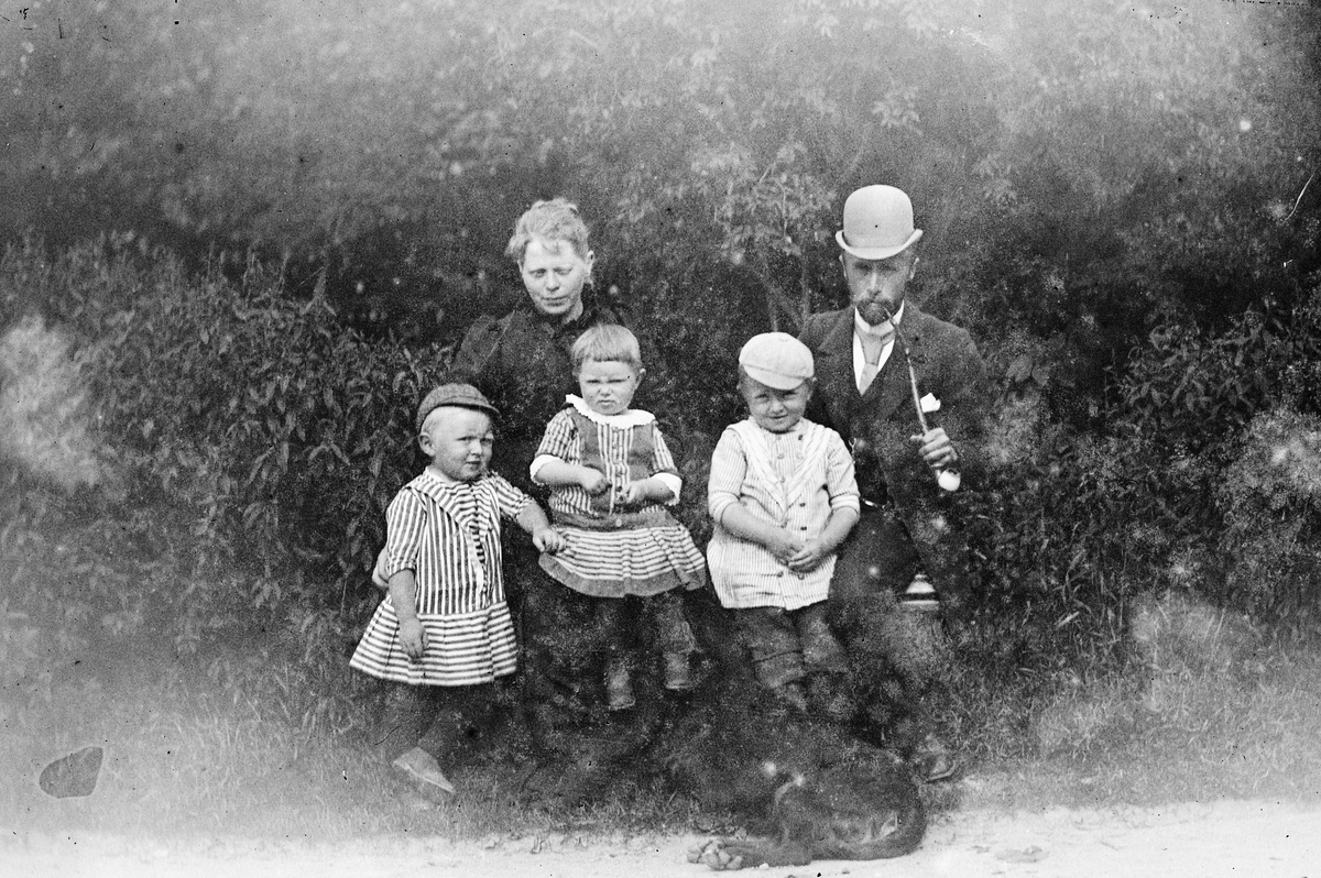 Hans Emil Erichsen, 2 voksne og 3 barn ute. Hund. Mannen røker pipe. Ukjente.