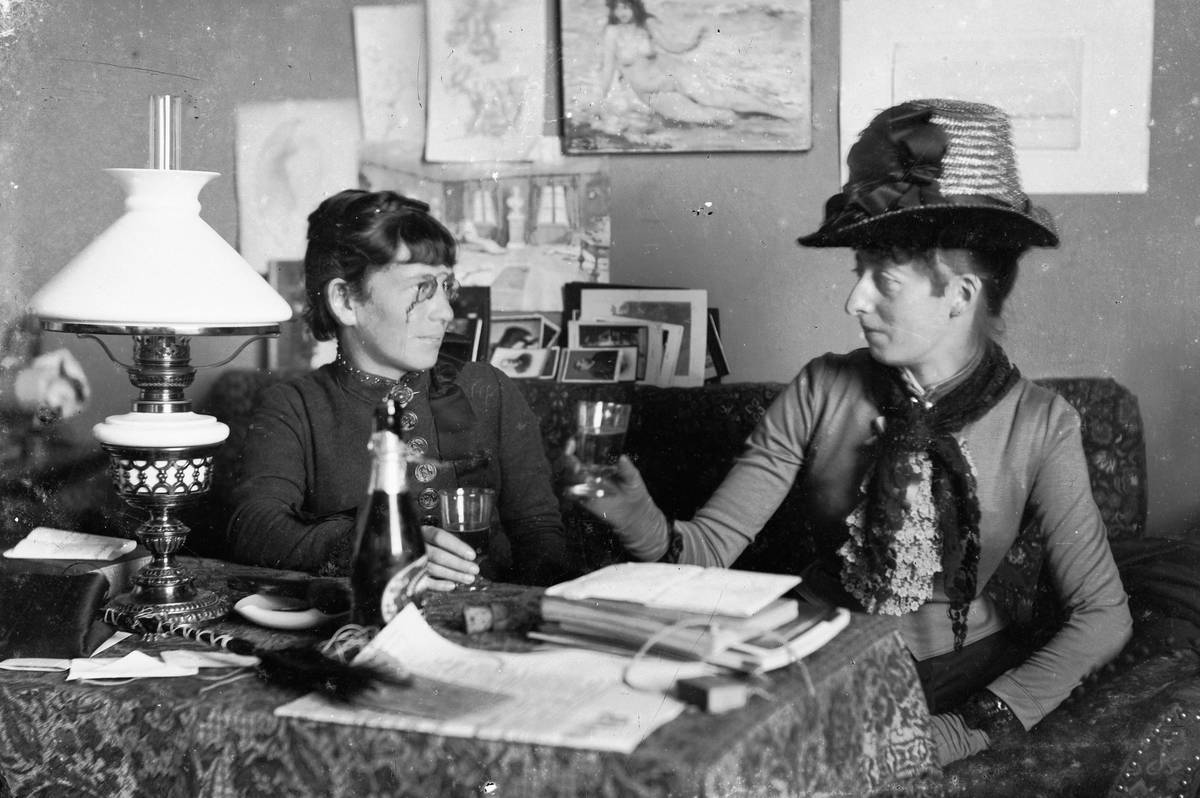 Hans Emil Erichsen, To kvinner skåler. Interiør stue. Damen til venstre er Vincentia Sofie Emma Guidotti Skramstad.
