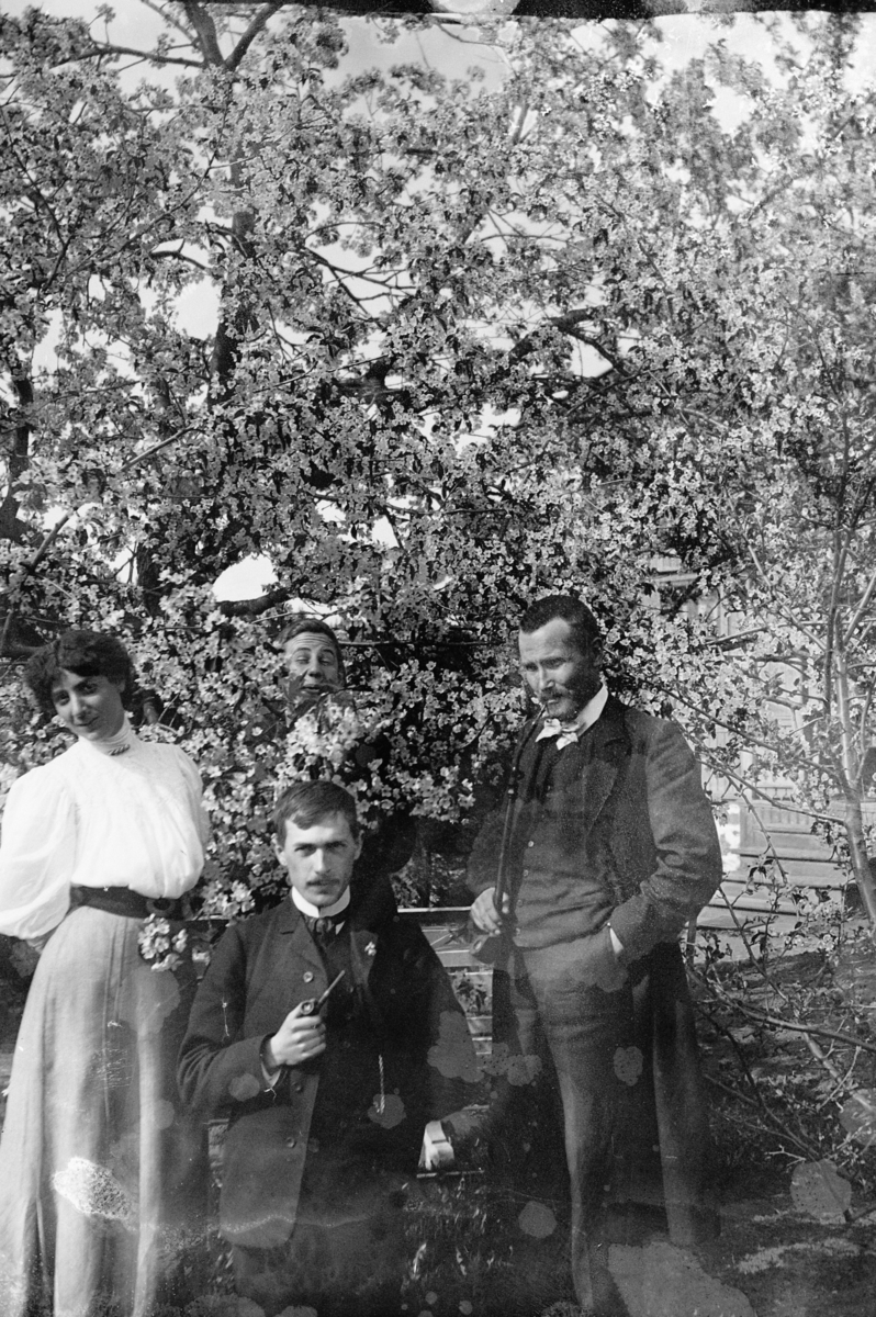 Hans Emil Erichsen, 3 ukjente menn og 1 kvinne ute i hagen. Frukttrær i full blomst.