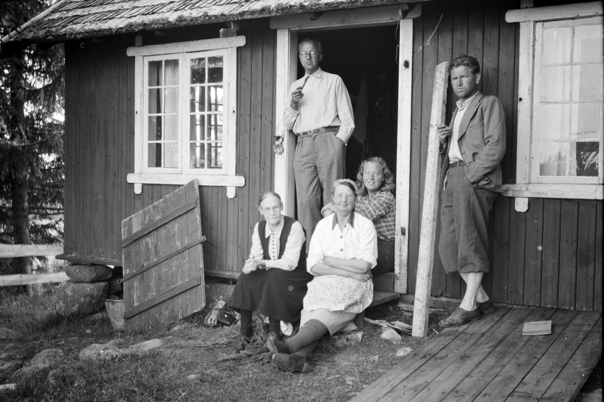Håkon Prestkværn, Familiegruppe Prestkværn på hytte på fjellet, sittende t. v. foran Gunda Prestkværn. Håkon Prestkværn står langs veggen mellom døra og vinduet. De øvrige ukjente.