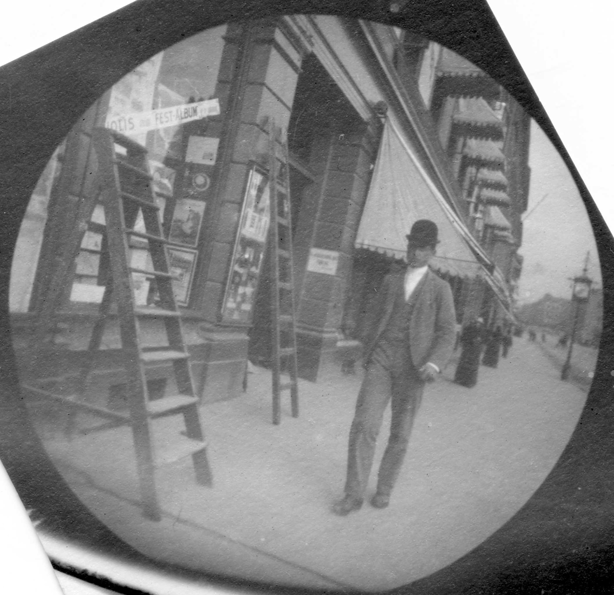 Fredrik Carl Mülertz Størmer, Thorvald Astrup spaserer på fortau langs butikker, Oslo. Markiser over vinduene, gardintrapp og stige mot vegg og vindu.