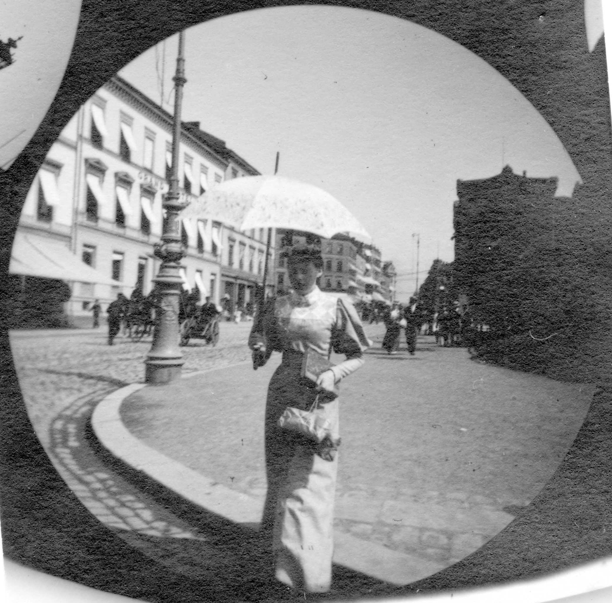 Fredrik Carl Mülertz Størmer, Frk. Andersen, gift l'Orange, med parasoll i ferd med å krysse Rosenkrantz` gate, Oslo. Stortinget i bakgrunnen.