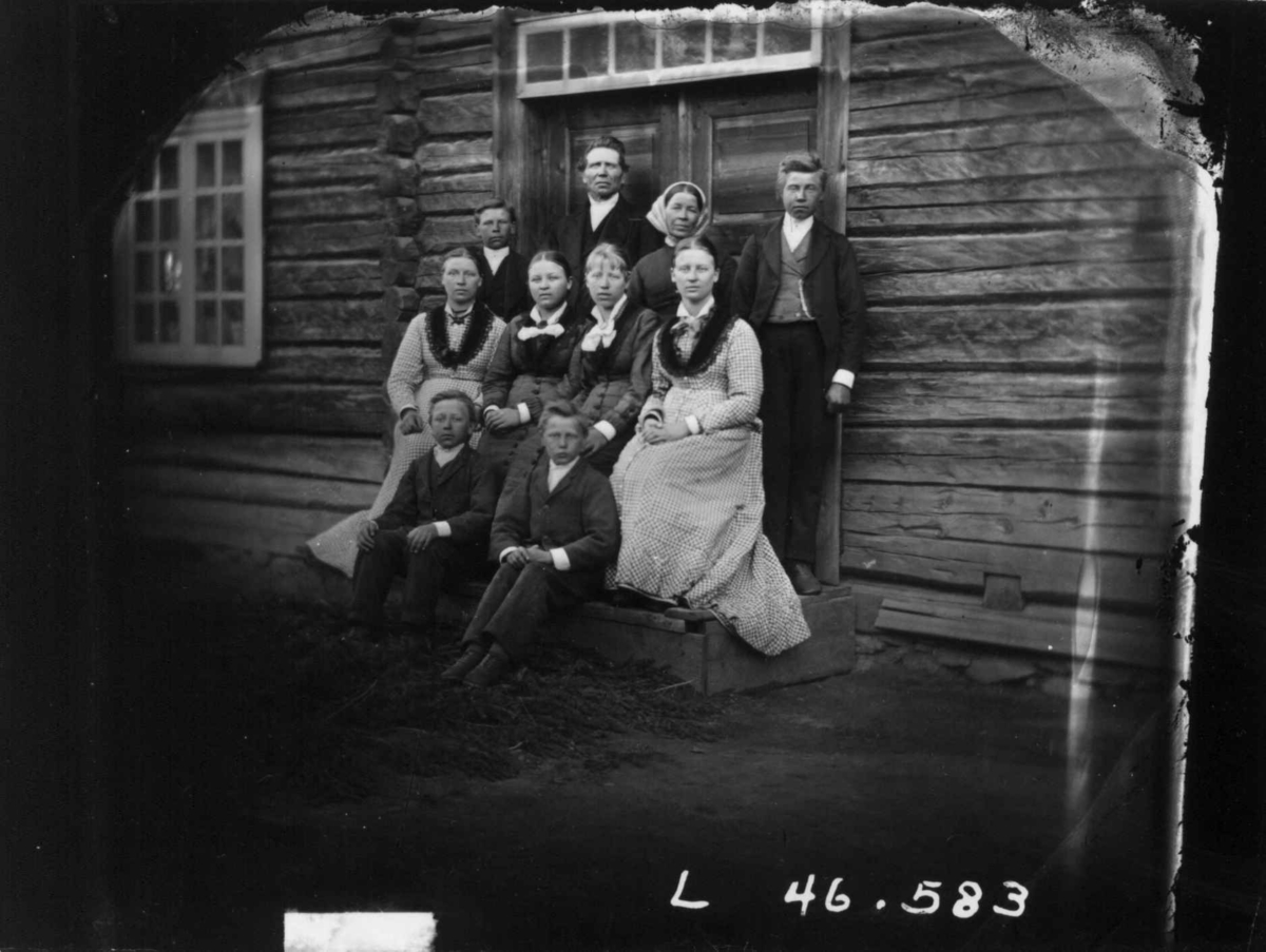Fredrik Emil Faye, Gruppeportrett, voksne og barn foran inngangsparti, Møllerstad, Ullensaker, ca. 1880. Gina Andersen Mon (?) med familien på Møllerstad. Fra portrettserie av personer som bodde på eller besøkte Dal gård, Ullensaker, fotografert av gårdens eier, kammerherre Fredrik Emil Faye (1844-1903) i årene 1875-…