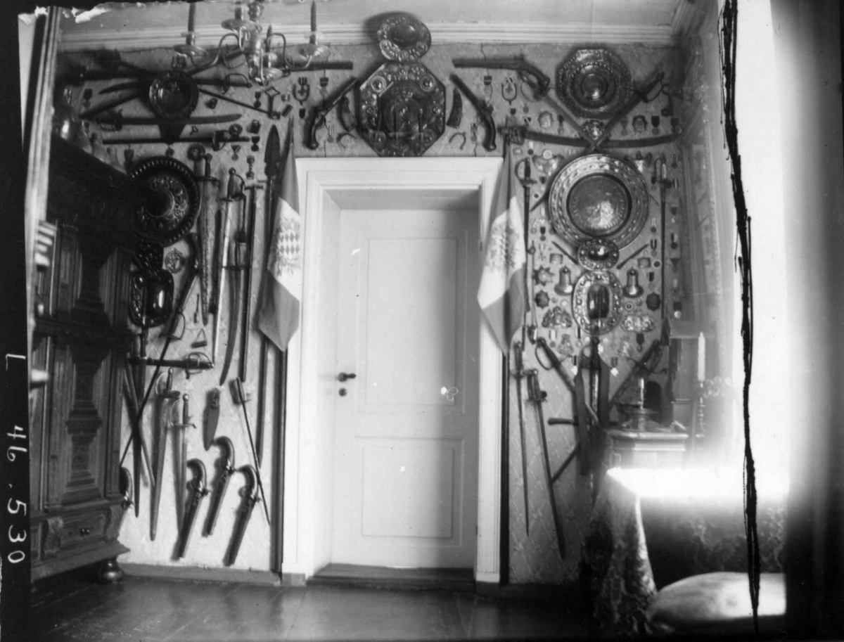 Fredrik Emil Faye, Interiør, Dal gård, Ullensaker. Vegg i gjennomgangsrom med opphengte våpen, skjold, taklampe. Ca. 1898. Fra serie fotografert av kammerherre Fredrik Emil Faye (1844-1903), gårdens eier.