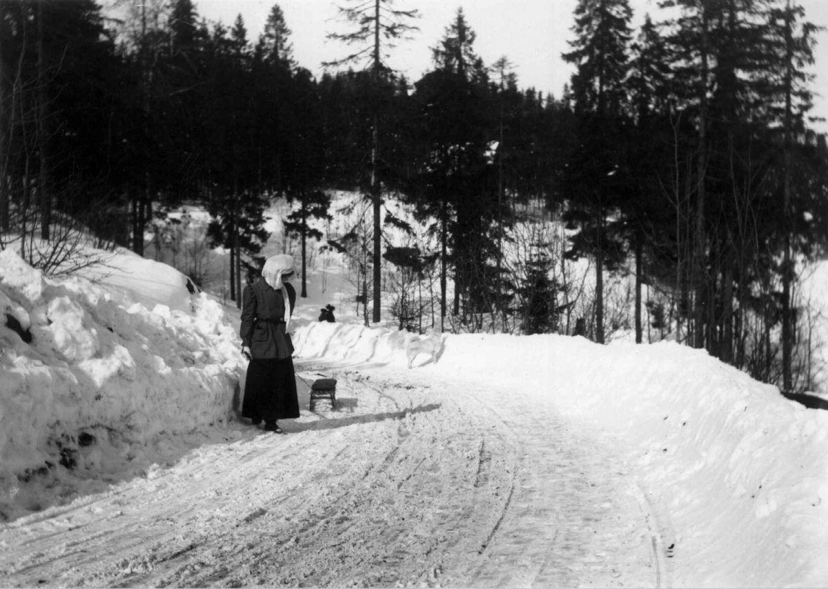 Hermann Christian Neupert, På vei til Holmenkollen. Wilhelmsøy. 1908-1910. Akende. Vintermotiv. Skog. Brøytet vei. Kvinne med kjelke.
