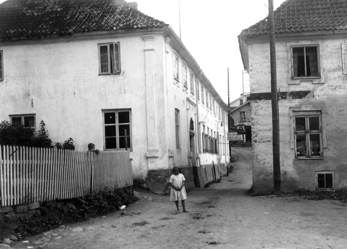 Hermann Christian Neupert, Son, Vestby, Akershus 1924. Bebyggelse. Smug med utsalg av bakervarer i bakgrunnen. En jente står i forgrunnen.