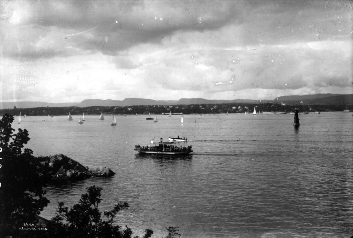 Hermann Christian Neupert, Indre Oslofjord, Oslo. Ferje fullsatt med passasjerer og seilbåter på fjorden. Bebyggelse i bakgrunnen.