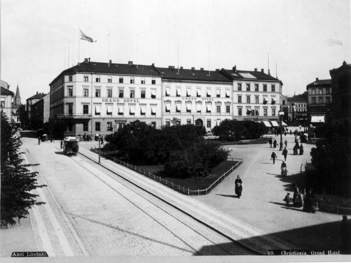 Axel Lindahl, Grand Hotel, Karl Johans gate, Oslo 1885-90. Gatebilde med hotellet, Eidsvoll plass, mennesker og hestetrikk. Sett fra Rosenkrantz' gate.