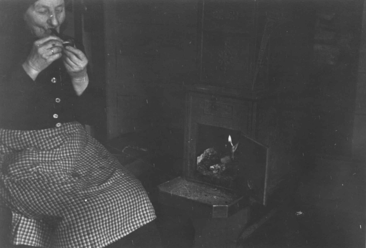 Anna Grostøl, Portrett av Anna Torsland som sitter ved siden av vedovnen. Åseral, Vest-Agder. 1943.