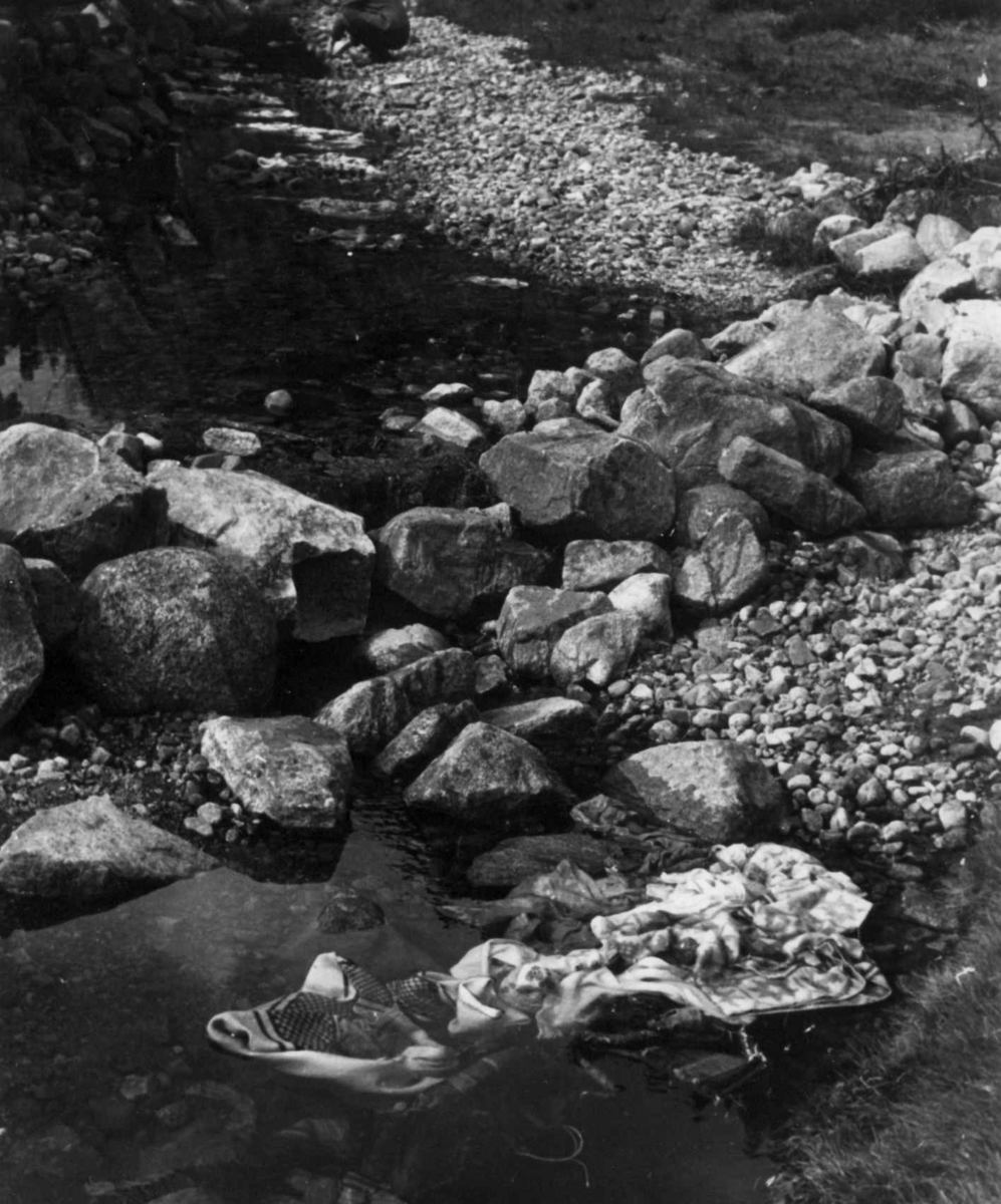 Anna Grostøl, Vasking av klær i kvernhusbekken på Smeland. Steiner er lagt oppå klærne så de ikke skal renne med strømmen. Åseral, Vest-Agder 1943.