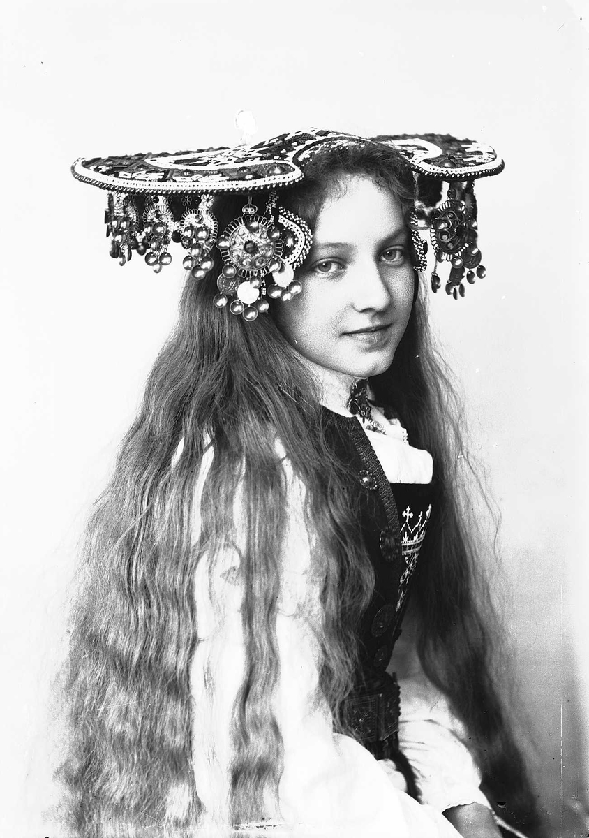 Solveig Lund, Studiofotografi av kvinne med brudedrakt og brudehatt på hodet. Sittende. Hofteutsnitt. Vendt mot høyre. Ser ut av bildet.