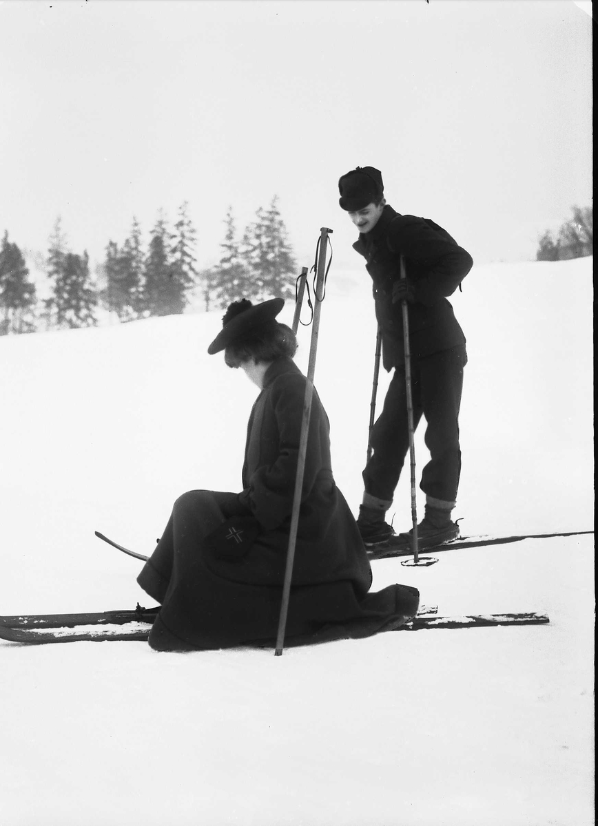 Solveig Lund, Mann og kvinne i snødekt landskap. Mann med ski på beina og sekk på ryggen. Kvinnen spenner på seg skiene.