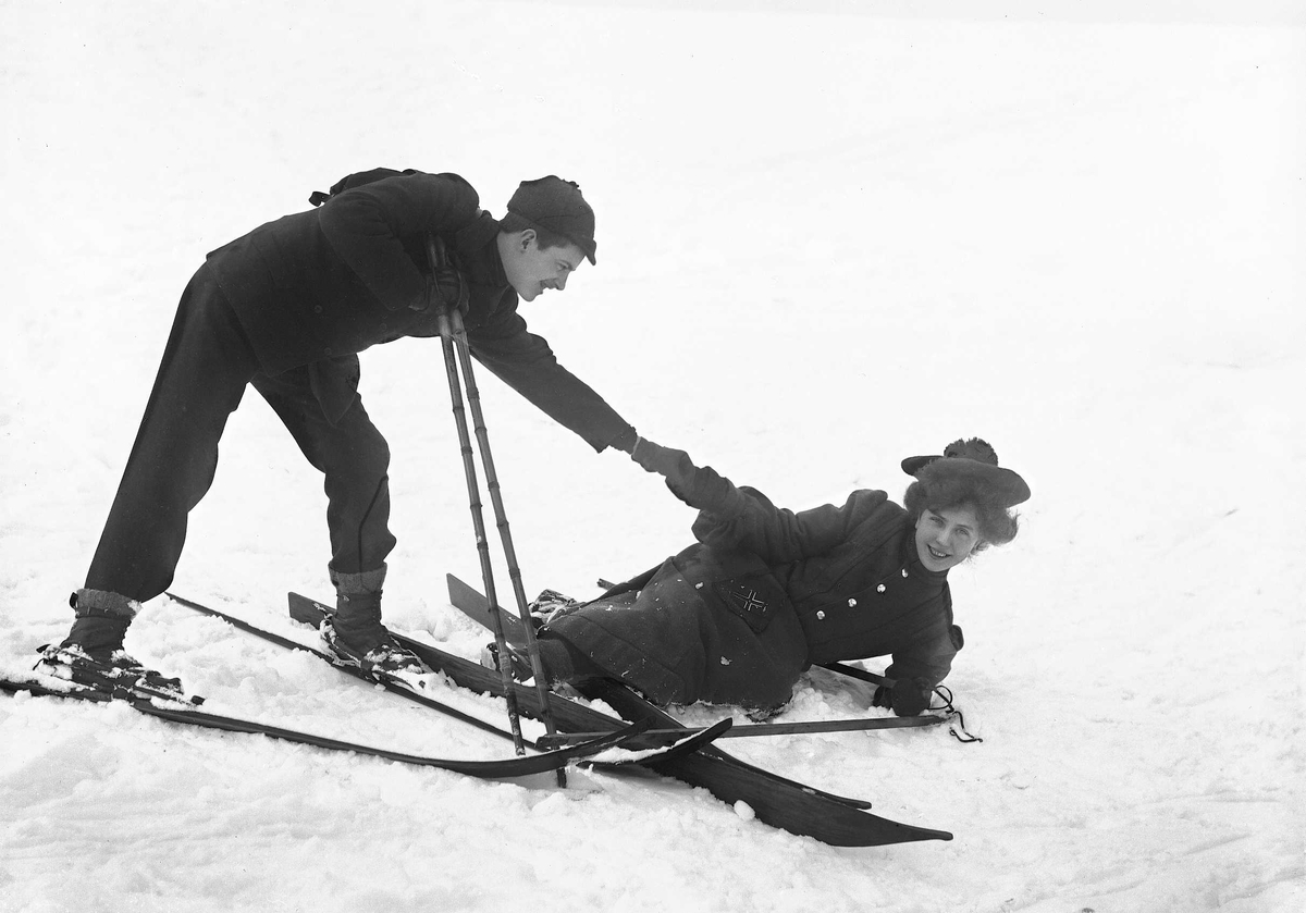 Solveig Lund, Kvinne og mann på ski i snødekt landskap. Mannen hjelper kvinnen opp etter et fall.
