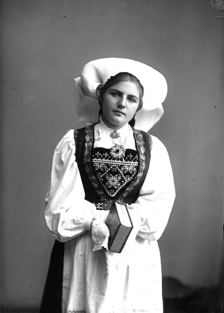 Solveig Lund, 3/4 dels studioportrett av kvinne i drakt, og skaut. Hun holder en bok i hendene. Bakgrunnen er nøytral.