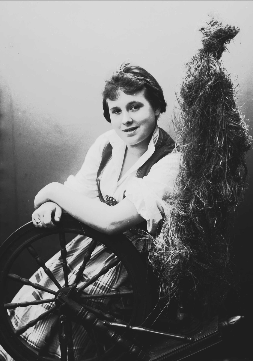 Solveig Lund, Studioportrett av kvinne i drakt, som sitter ved en rokk. Bakgrunnen er nøytral.