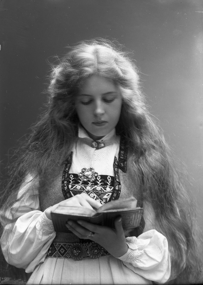 Solveig Lund, 1/2 dels studioportrett av kvinne i drakt med utslått hår. Hun holder en bok i hendene som hun leser i. Bakgrunnen er nøytral.