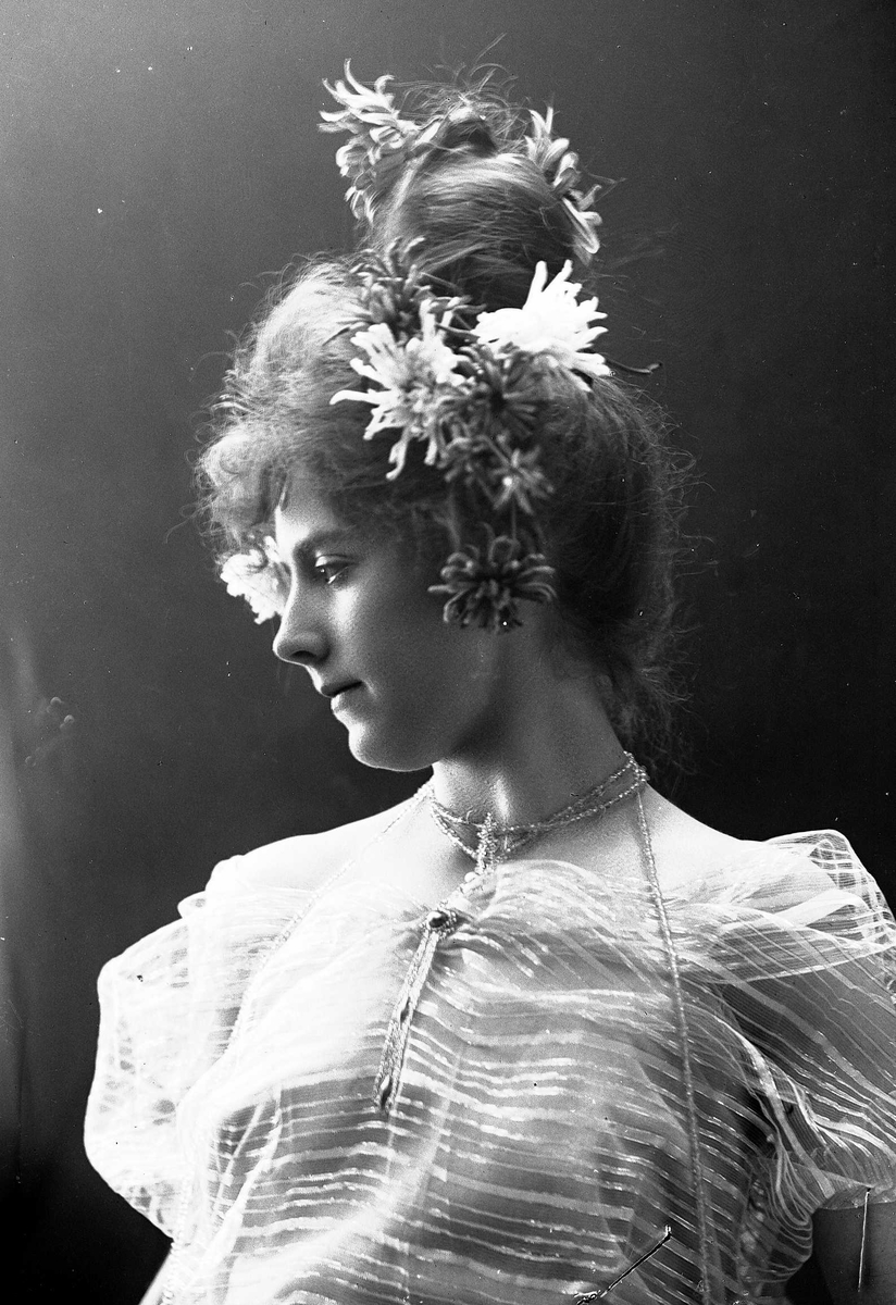 Solveig Lund, Studioportrett av kvinne i kostyme, oppsatt hår og halssmykke - hvit overdel og blomster i håret.