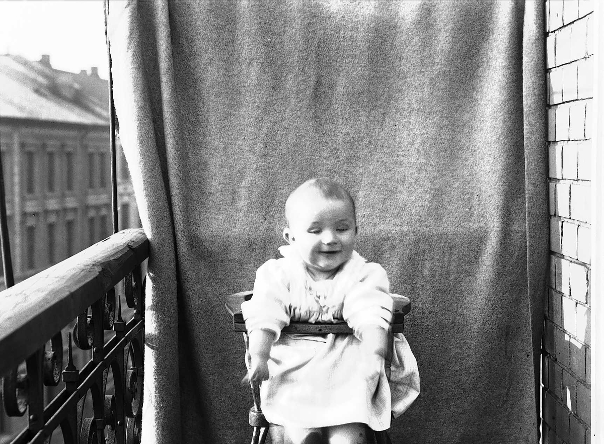 Axel Quinsgaard Wiborg, Lillebror Axel Q. Wiborg i barnestol på balkong, ant. Meltzers gate 9, Oslo, 1899. Fotografert mot opphengt bakteppe.