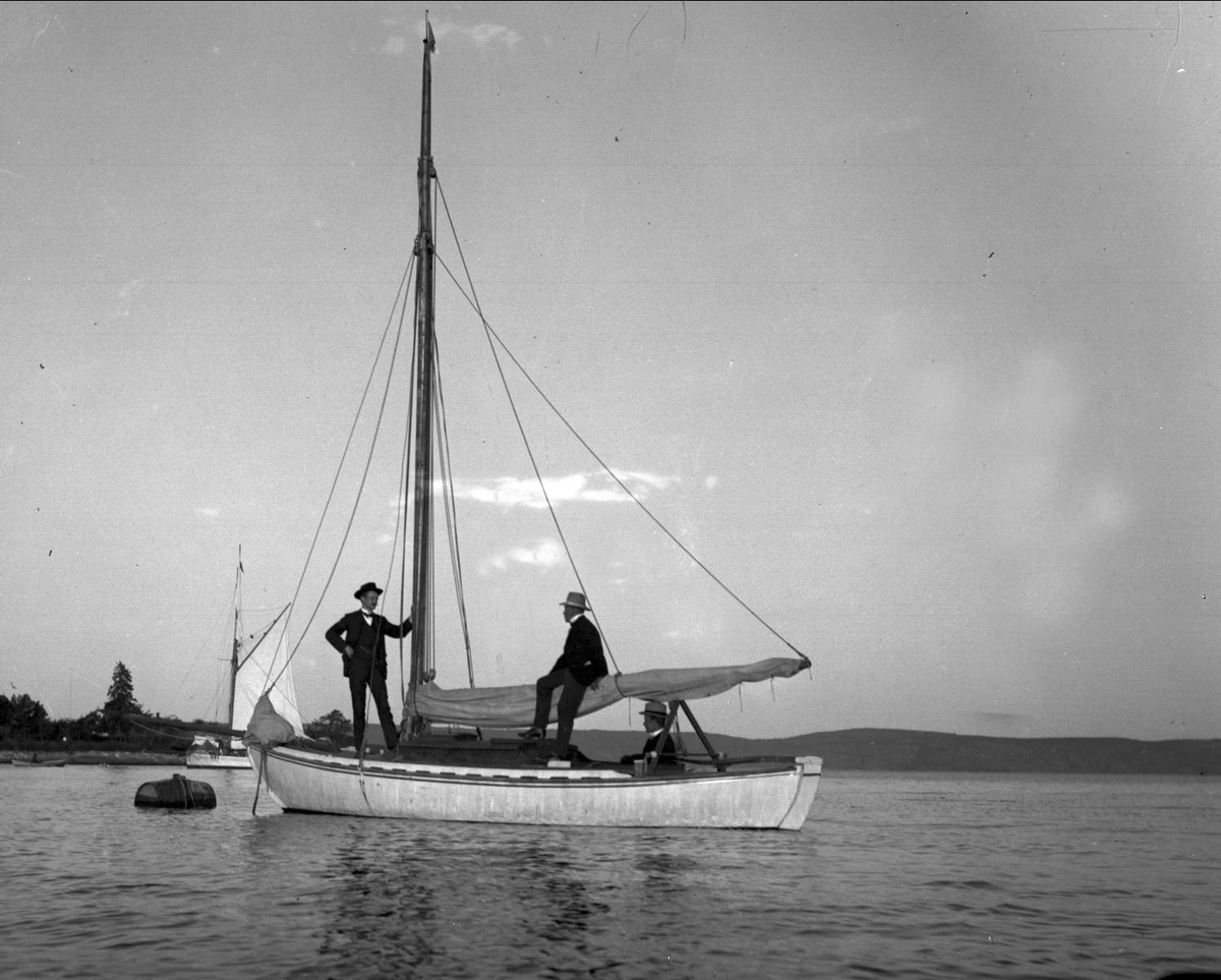 Gustav Borgen, Tre herrer i dress ombord liten seilbåt som er fortøyd. Juveler David-Andersen.