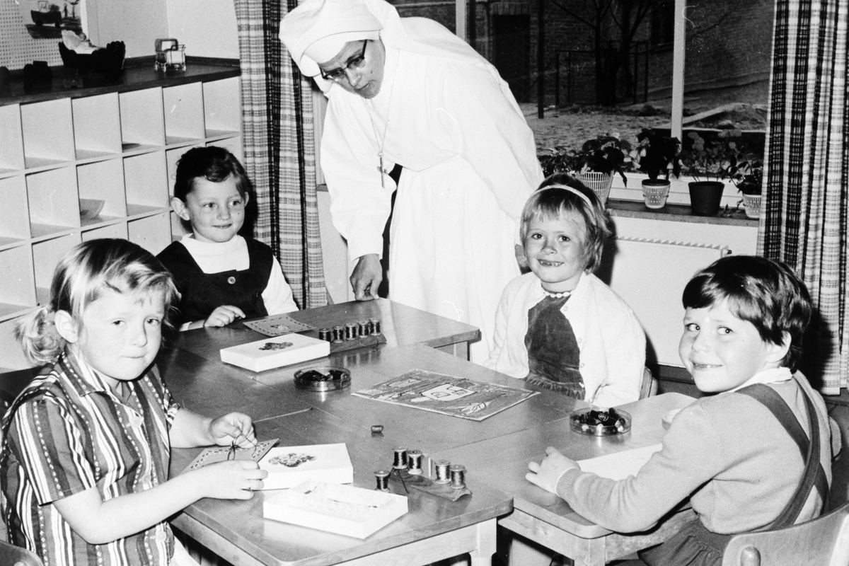 Anno Domkirkeodden, St. Torfinn menighet, Barnehage, Hamar. Gruppe ukjente barnehagebarn broderer. Ukjent søster sammen med barna i den nye bygningen som ble tatt i bruk 25. mai 1961.