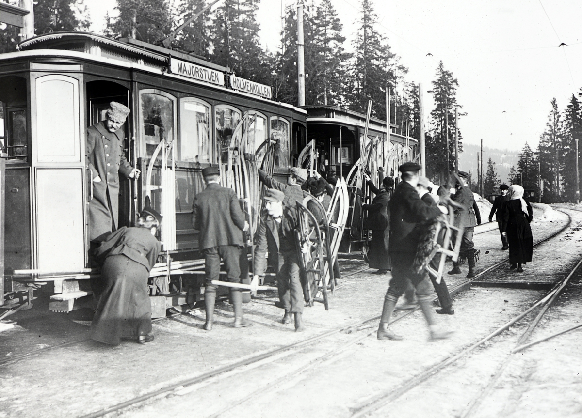 Anno Domkirkeodden, Holmenkollbanen, Oslo. T-bane. Trikk? Holmenkollen - Majorstuen. Holmenkollen stasjon. Folk med ski og kjelker, vinter.